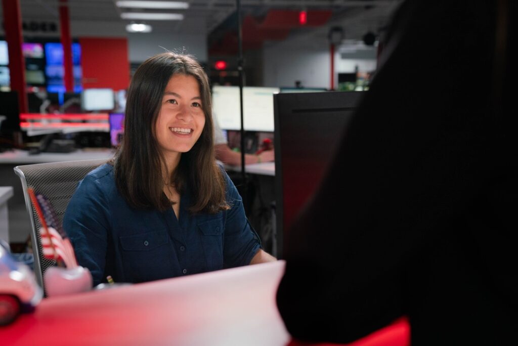 Jordan Hoover, who sits at an assignment desk, smiles at someone
